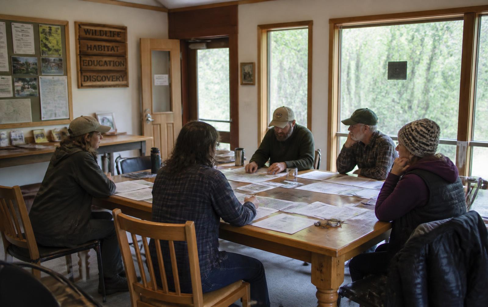 Trustees and staff deliberating over shared documents around a table in a nature center meeting room.