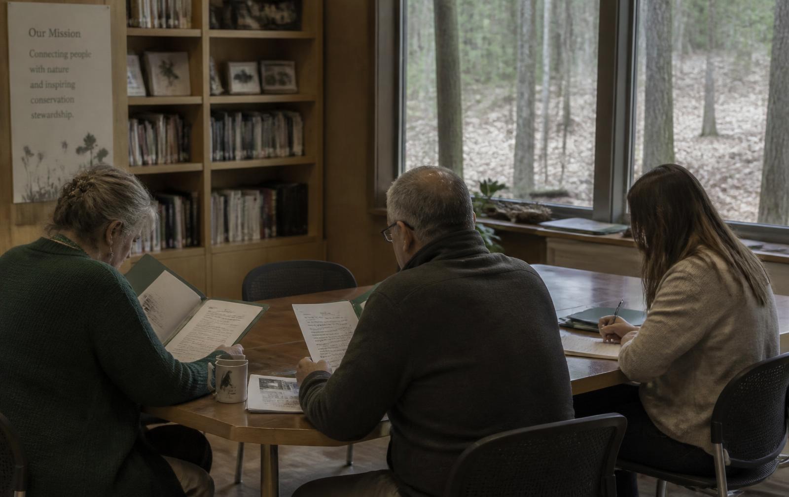 A small search committee reading candidate materials at a table in a nature center library.